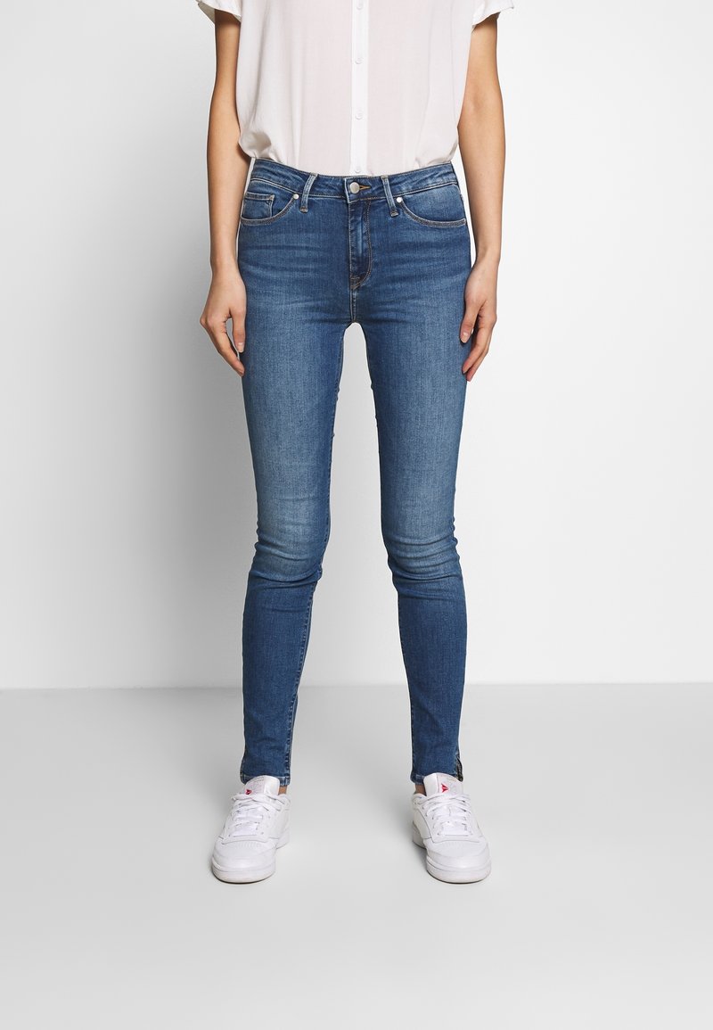 Dunne blauwe jeans met een gemiddelde wassing, gemaakt van denim. Bevat een knoop- en ritssluiting, vijf zakken en heeft een soepele textuur.