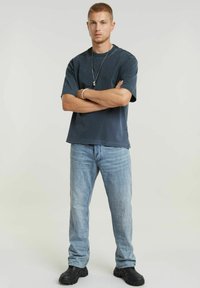 Tricou scurt, de culoare albastru închis, cu un croi lejer, purtat cu blugi de culoare albastru deschis și teniși groși negri. Accesorii simple, look curat.