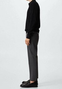 Schwarzer Strickpullover, graue maßgeschneiderte Hose, schwarze Slipper, Seitenansicht, die die Materialstruktur und elegante Designdetails zeigt.