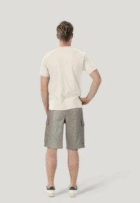 T-shirt beige in cotone abbinato a pantaloni cargo grigi con tasche laterali, completato con sneakers bianche per un look casual.