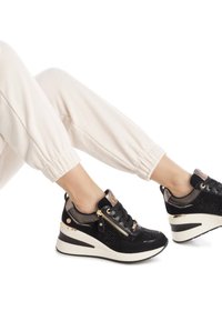 Zapatillas negras con una mezcla de materiales texturizados, que cuentan con un detalle de cremallera, paneles de malla y una suela de cuña. Detalles en hardware dorado.