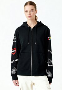 Felpa nera con zip e cappuccio con coulisse, caratterizzata da stampe grafiche di vari colori su maniche e petto, e una texture morbida in cotone.