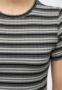 Κοντινό πλάνο ενός ατόμου που φοράει ριγέ κοντομάνικη μπλούζα με οριζόντιες μαύρες και λευκές ρίγες και στρογγυλή λαιμόκοψη.