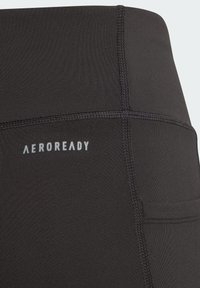 Leggings atléticos negros con tejido suave y elástico. Presentan costuras planas y un logo "AEROREADY" visible. Incluye un bolsillo lateral.