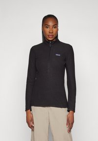 Black quarter-zip pullover, textured fabric, long sleeves, fitted design, featuring a small brand logo on the left chest.