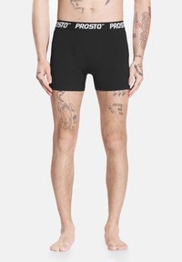Czarne bokserki z szerokim białym elastycznym pasem z napisem "PROSTO." Tkanina wydaje się gładka, dopasowana i elastyczna.