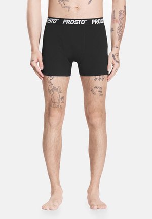 Czarne bokserki z szerokim białym elastycznym pasem z napisem "PROSTO." Tkanina wydaje się gładka, dopasowana i elastyczna.