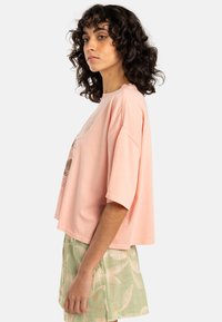 Rosa, oversized t-shirt med rund halsringning, korta ärmar och en grafisk tryck på framsidan. I kombination med gröna shorts med bladmönster.
