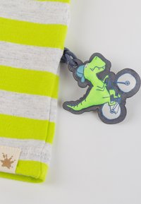 Graues und limonengrünes gestreiftes Stoffmuster mit einem Stoffetikett, auf dem ein grüner Dinosaurier auf einem Fahrrad abgebildet ist, hervorgehoben durch eine blaue Kappe und Räder.