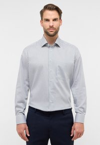 Camicia a righe bianca e blu navy, con colletto button-down, maniche lunghe e una tasca sul petto, dal tessuto complessivamente liscio.