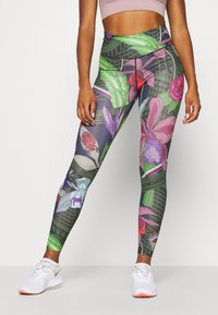 Personne athlétique portant des leggings taille haute avec des motifs floraux et de feuilles colorés, assortis à des baskets blanches et un crop top rose clair.