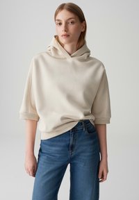 Licht beige hoodie met korte mouwen, een losse fit en een grote capuchon, gecombineerd met hoge taille blauwe denim jeans met een relaxte pasvorm.