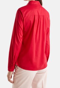 Camicia rossa a maniche lunghe in cotone, con colletto a bottoni, dettaglio di piega sul retro e polsini con bottoni. Vestibilità sagomata in vita.