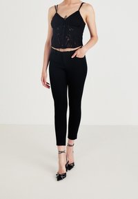 Černý kratký top s krajkovými detaily a nastavitelnými ramínky, doplněný úzkými černými kalhotami. Ozdobený vysokými podpatky s puntíky.