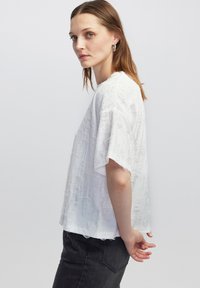 Witte top met korte mouwen van een gemêleerde stof met subtiele patronen. Zachte, losse pasvorm met raw edges en een relaxed fit.