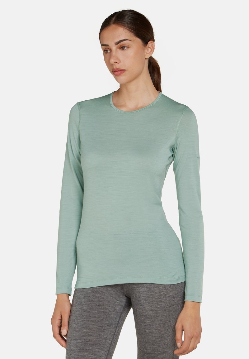 Top a maniche lunghe di un leggero verde chiaro realizzato in tessuto liscio, con scollo rotondo e vestibilità slim, abbinato a leggings grigi.