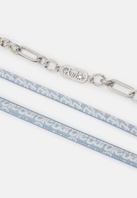 Hopeinen ketju, jossa on "Barbie"-logo ja strassikoristeita, yhdistettynä kahteen vaaleansiniseen hihnaan, joissa on reunakuvioitu kuvio.