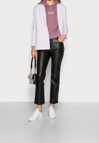 Blazer lila claro sobre una sudadera color malva, pantalones de cuero sintético negros y zapatillas blancas. El conjunto incluye un pequeño bolso negro.
