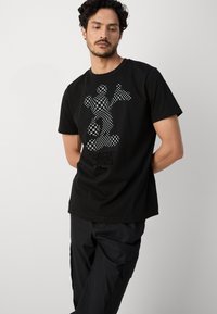 Camiseta de algodón negra con un gráfico de Mickey Mouse de cuadros en la parte posterior. Mangas cortas, escote redondo y corte holgado.