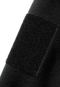 Gros plan sur un tissu noir avec un patch rectangulaire en scratch cousu sur une surface texturée.