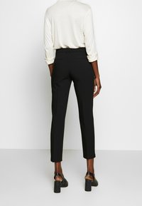 Zwarte op maat gemaakte broek met een slanke pasvorm, voorzien van een gladde textuur en een tailleband. Gecombineerd met een lichtgekleurde top met lange mouwen.