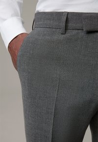 Grijze op maat gemaakte broek met een subtiele textuur, voorzien van zijzakken en een platte tailleband. Gepaarde met een witte blouse met lange mouwen.