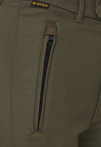 Olivgrön byxor med en dragkedjeficka med svart dragkedja, kraftig tygkvalitet och en liten G-Star-logotyp vid midjan.
