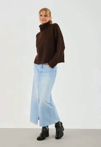 Kahvivärinen ribbed turtleneck-neule, vaaleansiniset leveät farkut, mustat nilkkurit hopeisella sisustuksella, seisomassa neutraalilla taustalla.