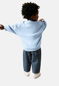 Sudadera azul claro con hombros caídos, combinada con pantalones holgados de cuadros azul marino y blanco y zapatillas blancas.