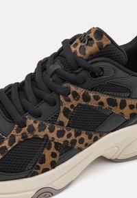 B baskets noires avec un mélange de mesh et d'accents en fourrure léopard, des lacets noirs et une semelle texturée avec une semelle intermédiaire beige.