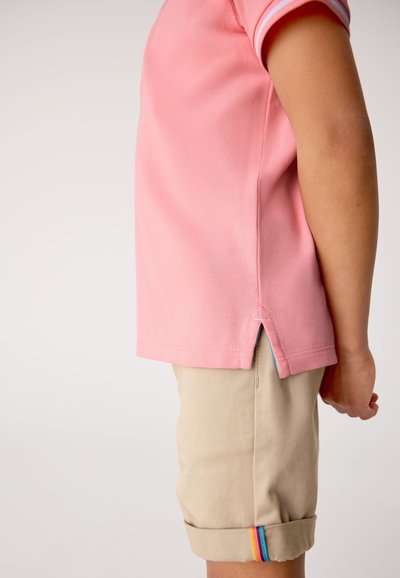 Lichtroze poloshirt met korte mouwen en contrasterende gestreepte manchetten. Gecombineerd met beige korte broek, omgeslagen zomen met regenboogaccent.