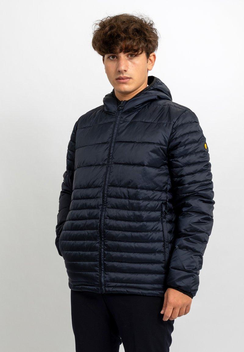Giacca puffer blu navy con motivo a righe orizzontali, zip frontale e cappuccio. Realizzata in materiale lucido e leggero, con un accento logo.