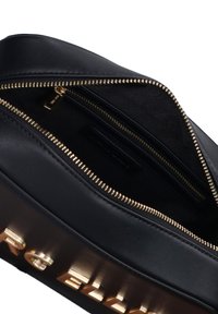 Interno di una borsa in pelle nera con dettagli in cerniera dorata, dotata di un ampio scomparto principale e di una tasca laterale per l'organizzazione.