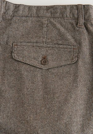 Pruun mustriga kangas väikese ruudustiku disainiga, kus on tagatasku pruuni nupuga. Sile tekstuur ja kohandatud sobivus.