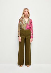 Camicia a fantasia floreale verde e rosa, con un grande colletto e bottoni, abbinata a pantaloni larghi a vita alta in verde oliva.