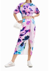 Sada dvoudílného háčkování s květinovým vzorem, která zahrnuje top s krátkými nabíranými rukávy a dlouhou sukni s bočním rozparkem. Barevné odstíny růžové, fialové a modré.