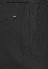 Svarta linnebyxor med elastisk midja, utrustade med en sidoficka och en diskret varumärkestagg. Mjuk textur med matt finish.