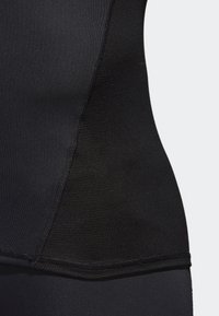 Haut de sport noir au design ajusté, tissu texturé et coutures lisses le long des coutures, mettant en valeur une silhouette élégante.