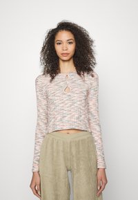 Top cropped de manga longa em tecido texturizado nas cores rosa, cinza e branco, com duas aberturas circulares na gola, combinado com calças de sarja beije claro.