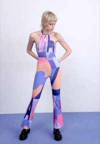 Farebný halter top s geometrickými vzormi v odtieňoch ružovej, modrej a fialovej; kombinovaný s vyhovujúcimi rozšírenými legínami a čiernymi platformovými topánkami.