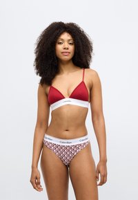 Ερυθρό ριγωτό τριγωνικό σουτιέν με ρυθμιζόμενες τιράντες. Συνοδευτικό σλιπ hipster με λουλουδάτο μοτίβο και λευκή ελαστική μέση με την επιγραφή "Calvin Klein".