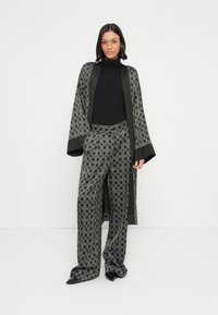 Hall triibuline kimonoga, millel on kellukakujulised varrukad ja sobivad laiad püksid geomeetrilise mustriga, kantud koos musta kõrge kaelusega ning teravate kontsadega.