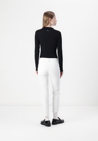 Crna rebrasta majica dugih rukava s prilagođenim dizajnom, u kombinaciji s bijelim uskim trapericama do gležnjeva. Cijeli outfit upotpunjuju crne cipele.
