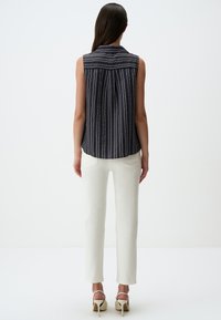 Blusa senza maniche blu navy con righe verticali bianche, colletto, retro plissé, abbinata a pantaloni bianchi a gamba dritta e sandali con tacco beige.