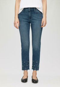 Jean en denim bleu à coupe droite, doté d'un ourlet effiloché orné de fausses perles blanches et d'un style classique à cinq poches.