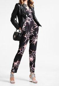 Svart blommig jumpsuit med rosa detaljer, parat med en svart läderjacka, grå klacksandaler och en liten svart handväska.