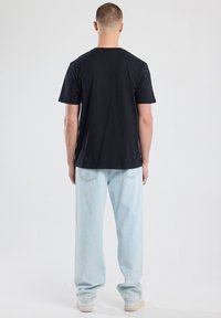 Camiseta negra de manga corta con cuello redondo clásico, combinada con jeans de corte holgado en azul claro y zapatillas blancas. Diseño sencillo y sin adornos.