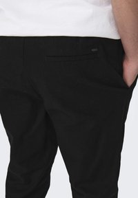 Svarta byxor med en strukturerad passform, med en bakficka med en subtil sömdetalj, och en slät tygtextur.