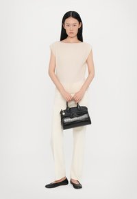 Black textured handbag with dual handles and a gold hardware accent, paired with light, ribbed top and light pants, worn with black flats.