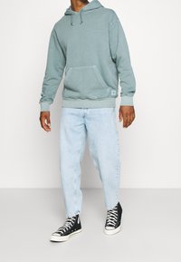 Ljusblå, oversize hoodie med känguruficka och huva med dragsko, kombinerad med ljusa denimjeans och svarta höga sneakers.